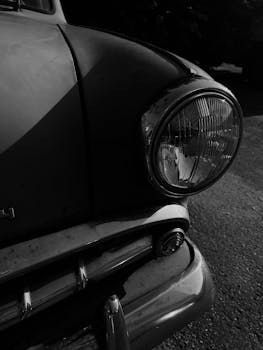 Artistic black and white close-up of a vintage car headlight and grille, evoking nostalgia.