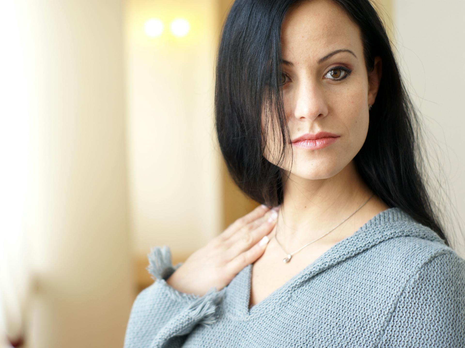 A woman with long black hair and a grey sweater