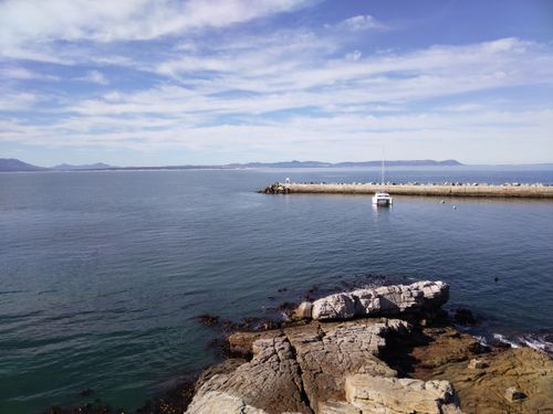 Free Serene coastal scene with rocky shore, calm waters, and sailboat under blue sky. Stock Photo