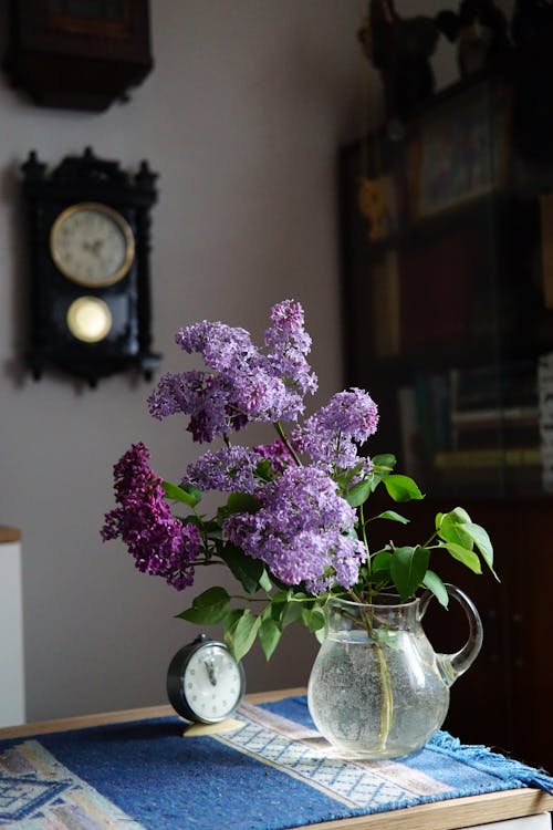 A vase of flowers sits on a table next to a clock