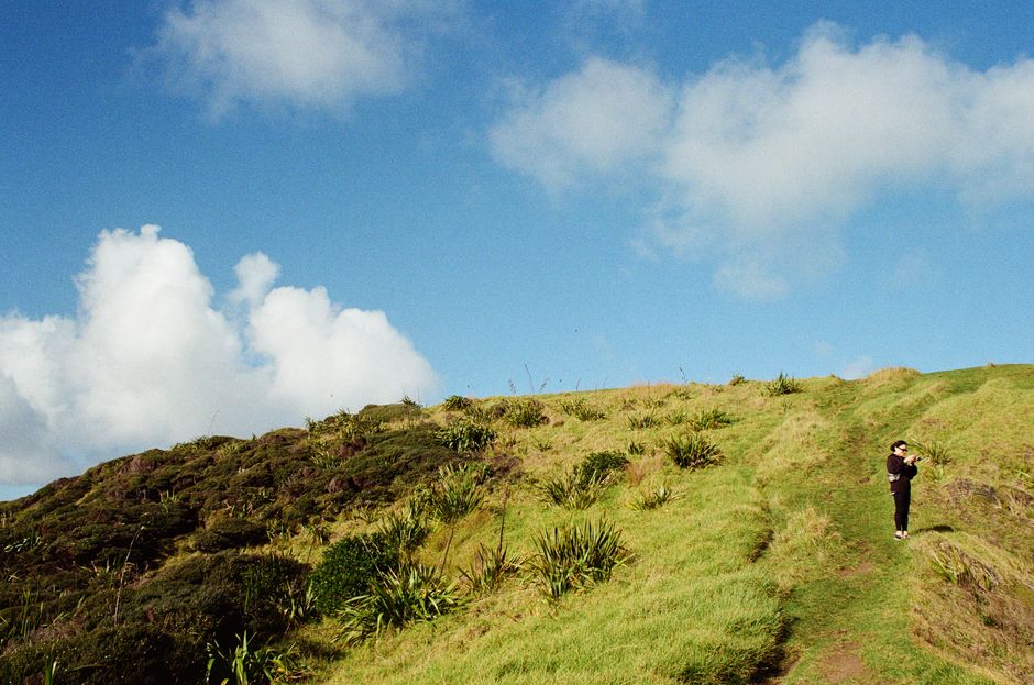A lone hiker explores a grassy hilltop under a bright blue summer sky.