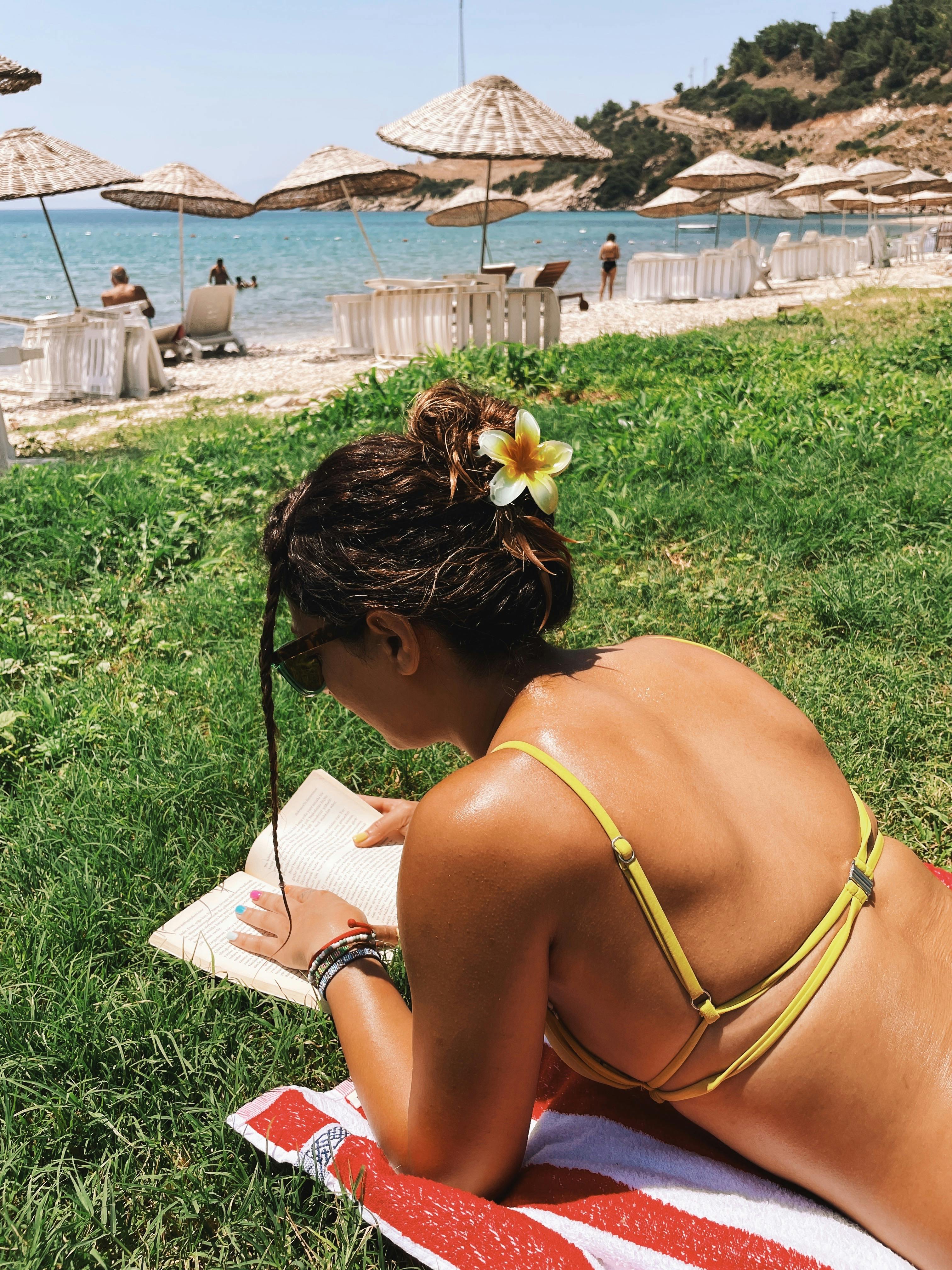 Woman in bikini reading on the beach under sunny skies. Perfect summer relaxation moment.