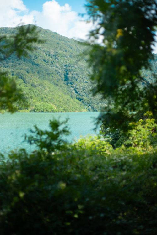 Free Tranquil lake view with lush green hills under a bright blue sky. Stock Photo
