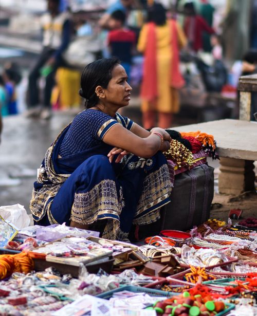 Free An Indian woman vendor sits at her colorful street stall selling handmade goods at a bustling market. Stock Photo