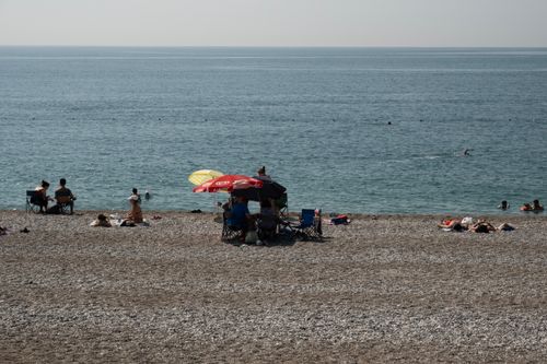 Free A serene beach scene with people relaxing under umbrellas on a pebble shore facing the ocean. Stock Photo