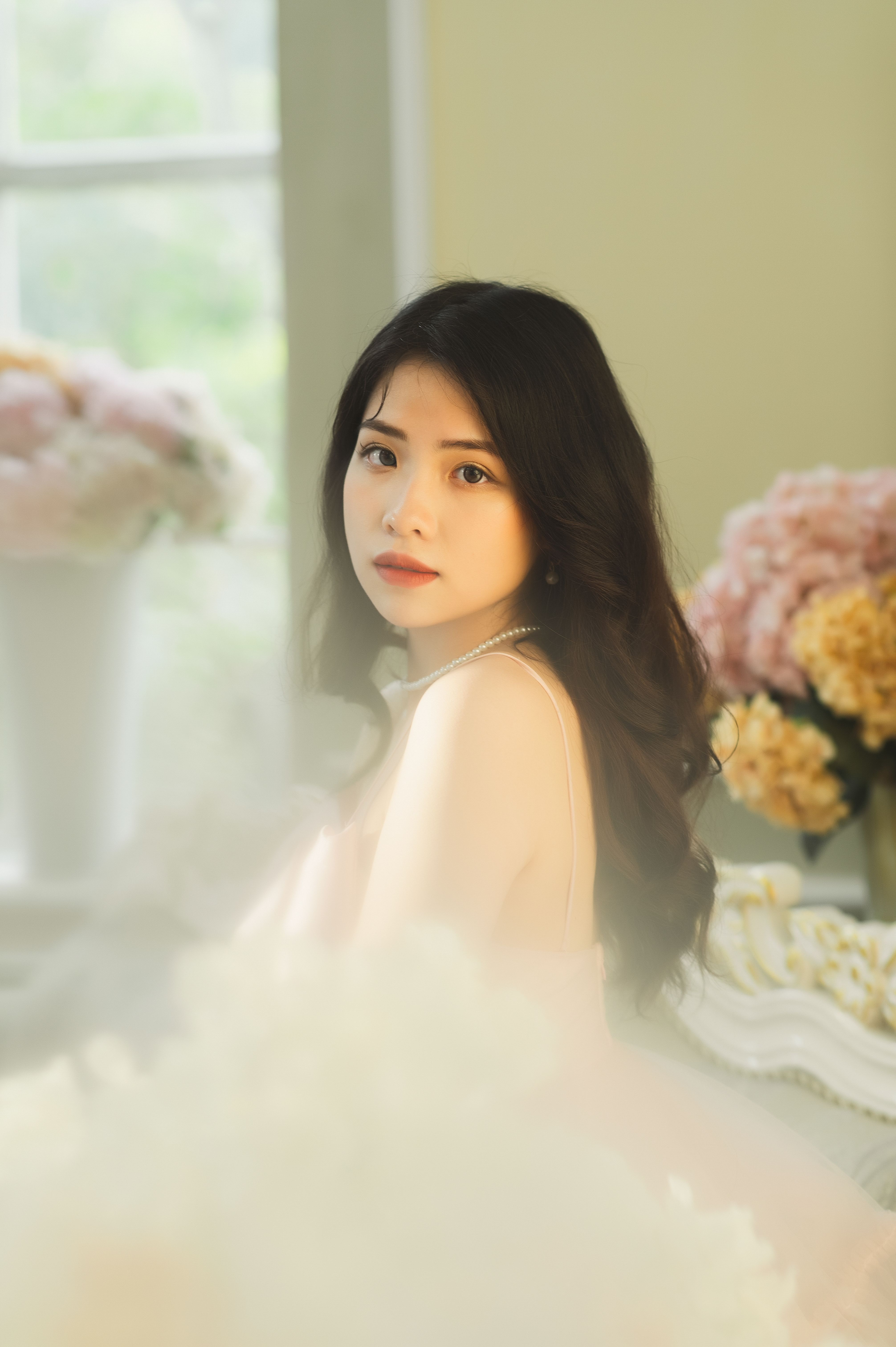 A beautiful bride in an elegant dress posing indoors with a soft floral background.
