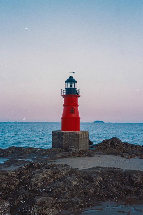 A red lighthouse on a rocky shore with the ocean in the background