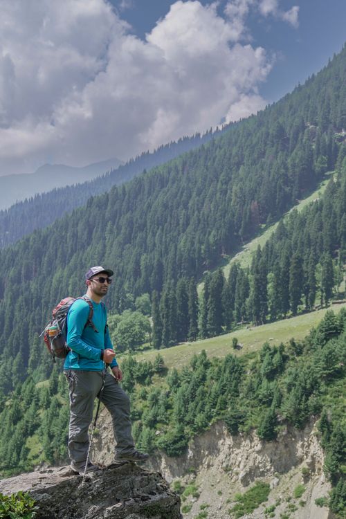 Free Male hiker with a backpack standing on a rock, enjoying the scenic mountain views. Stock Photo