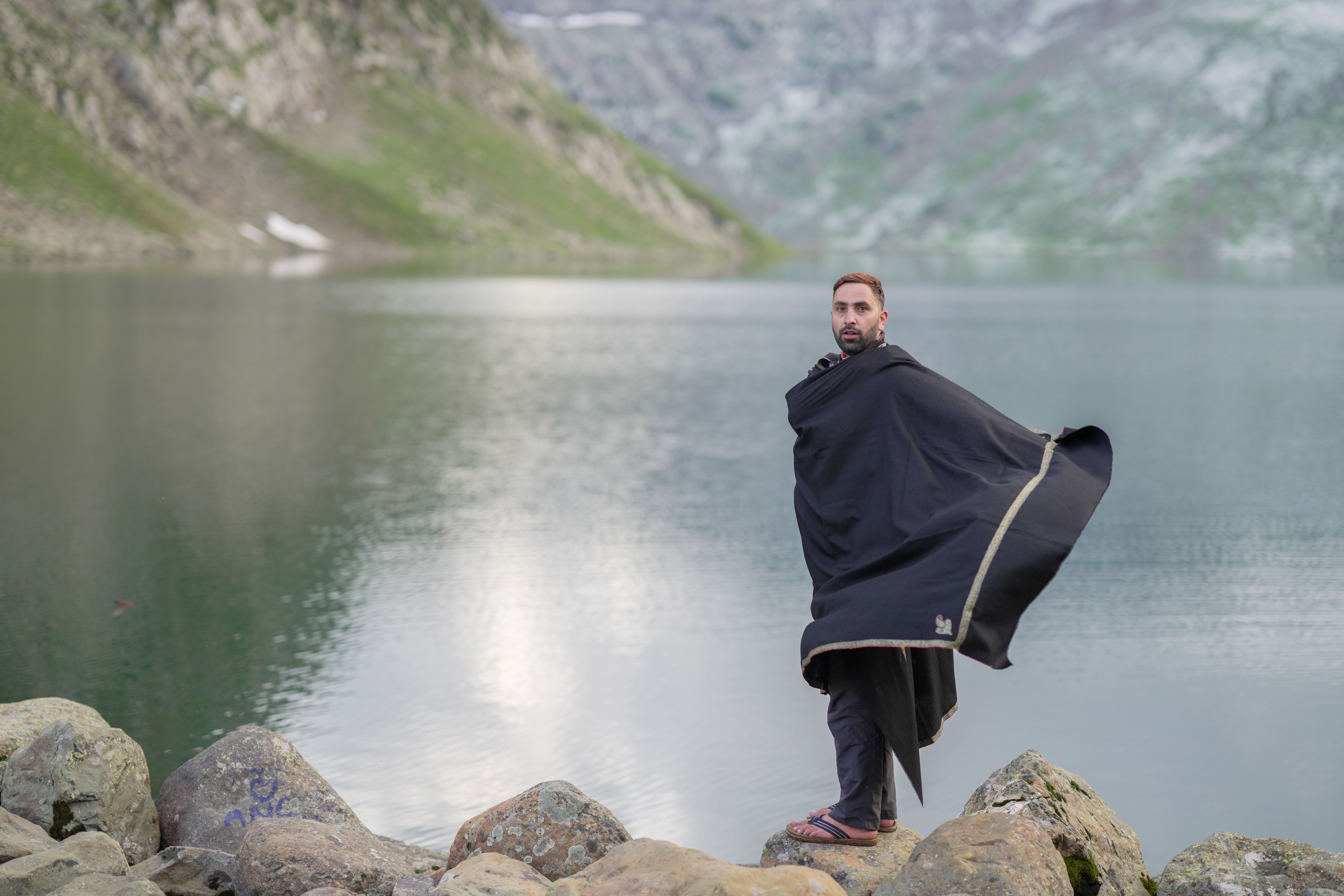 A man standing on rocks by a lake wearing a black blanket · Free Stock ...