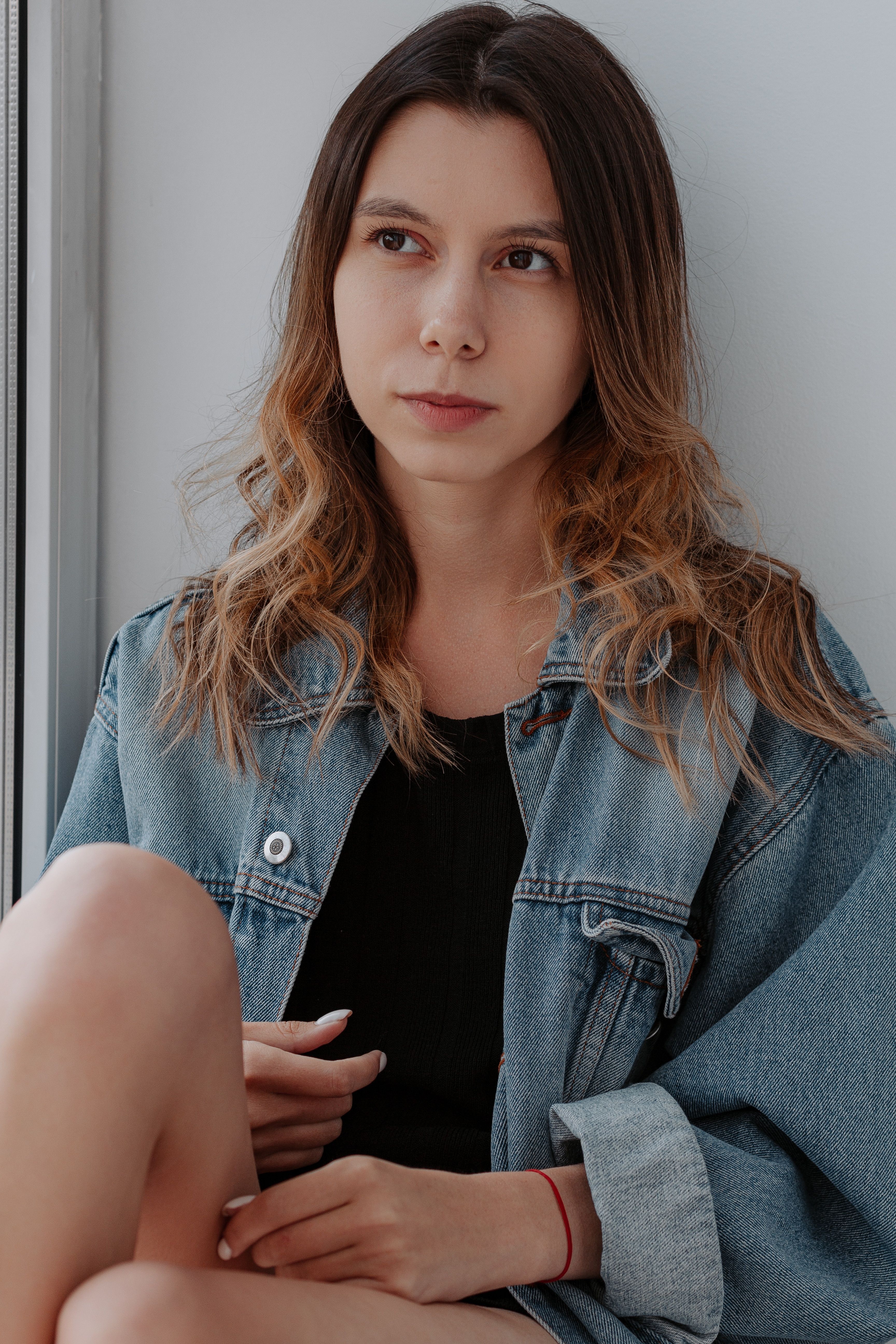 A woman in a denim jacket sitting on a window sill · Free Stock Photo