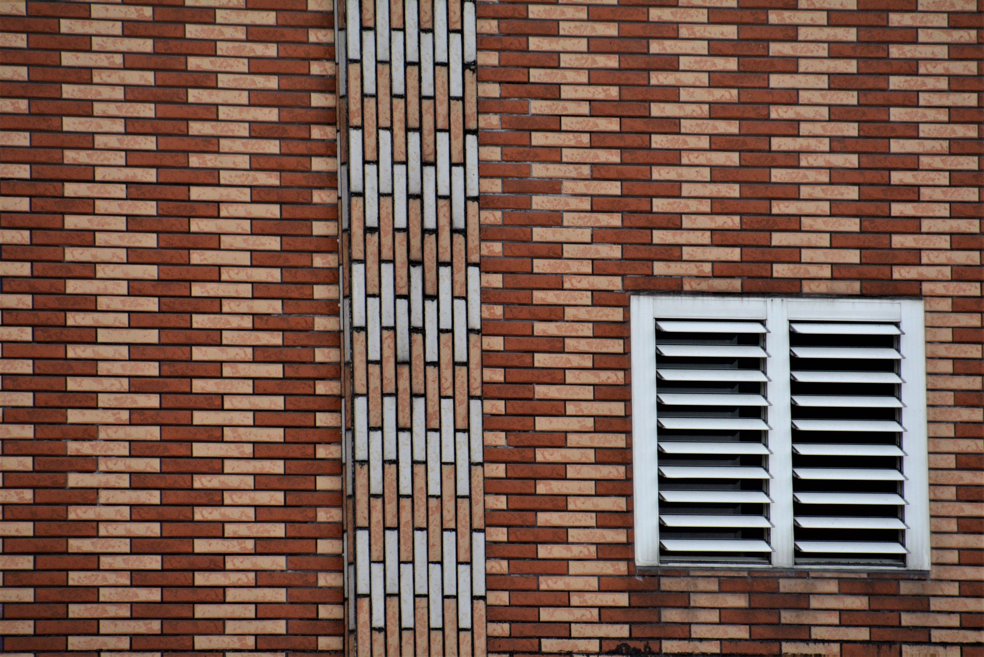 A brick wall with a window and a white shutter