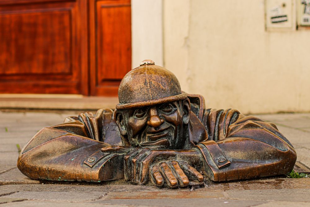 Statuia de bronz a unui bărbat care iese dintr-o gură de canal, pe o stradă din Bratislava