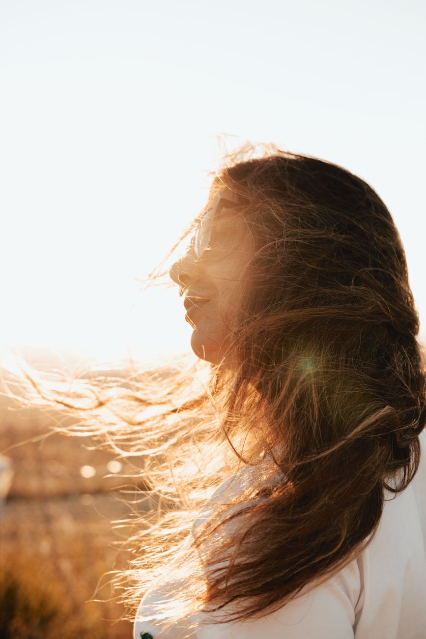 Woman enjoying the sunset with her hair flowing in the wind, capturing the essence of summer.