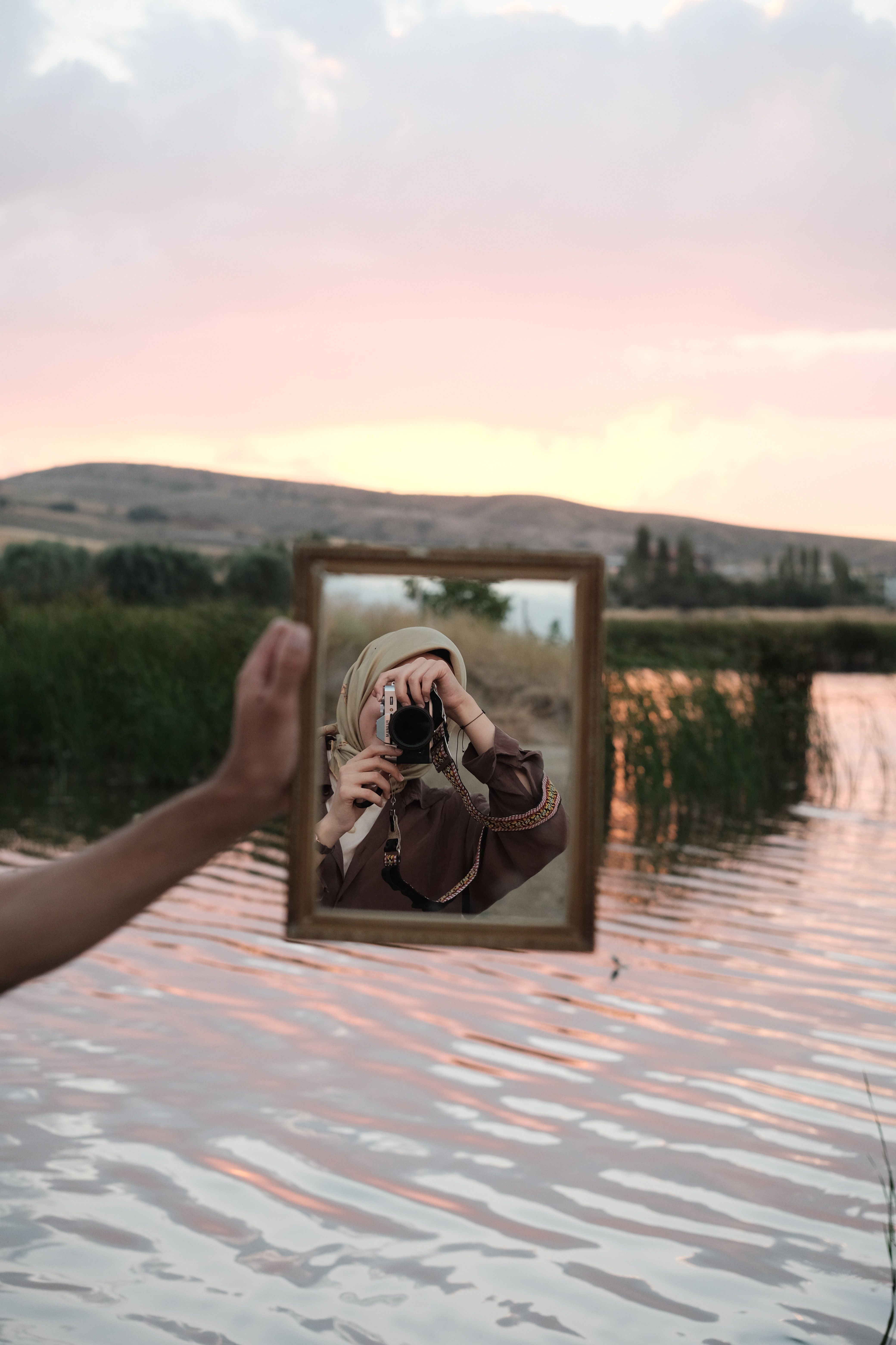 A serene reflection in a hand-held mirror by the lake during a vibrant sunset.