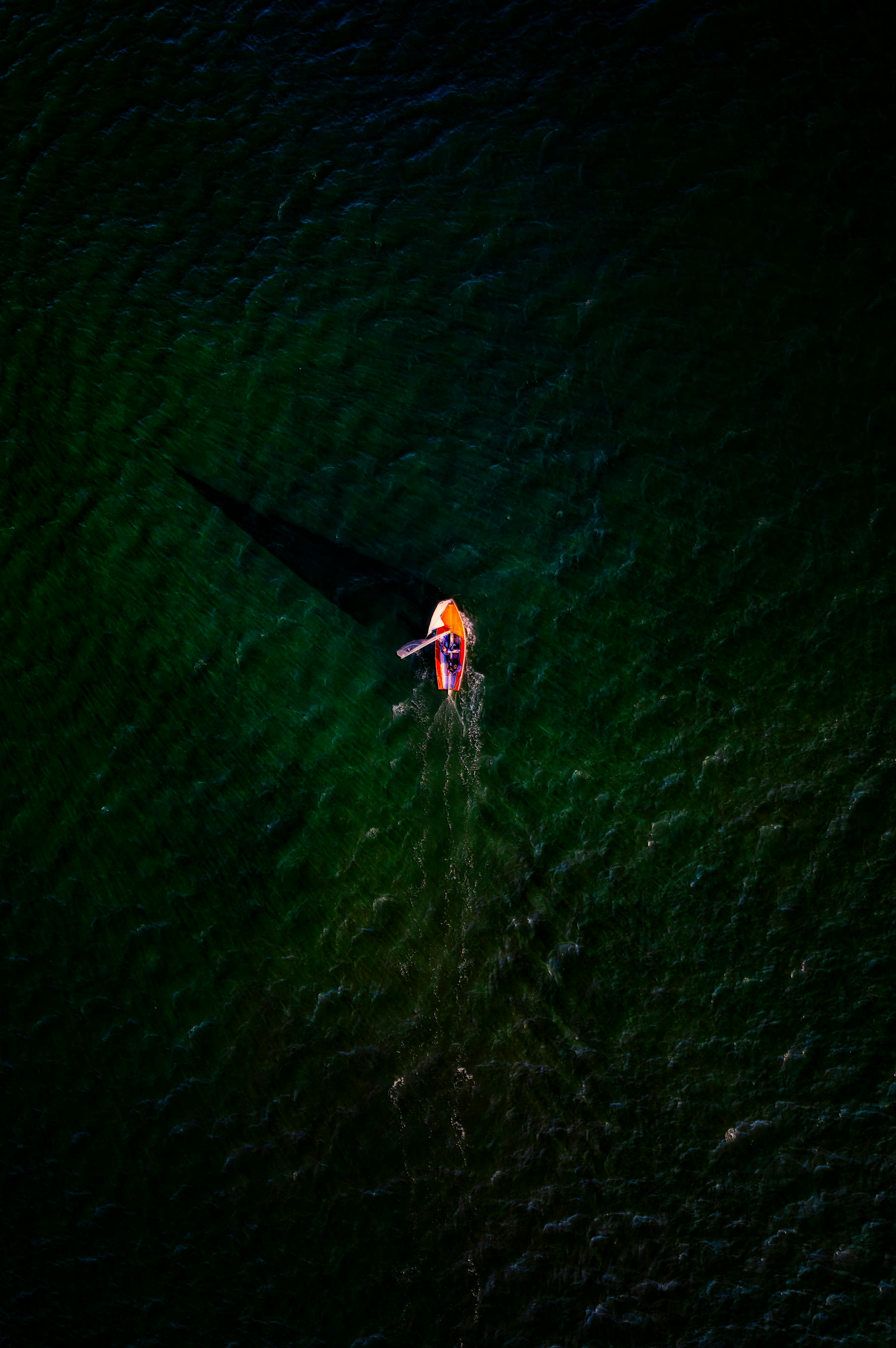 A sailboat casting a shadow in green ocean waters, captured from above in Sidmouth, UK.