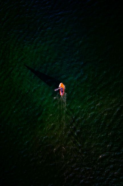 A sailboat casting a shadow in green ocean waters, captured from above in Sidmouth, UK.