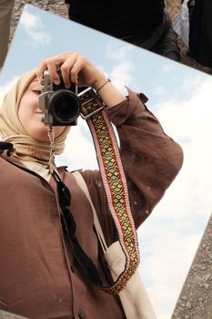 A person takes a selfie using a camera with a stylish strap outdoors.