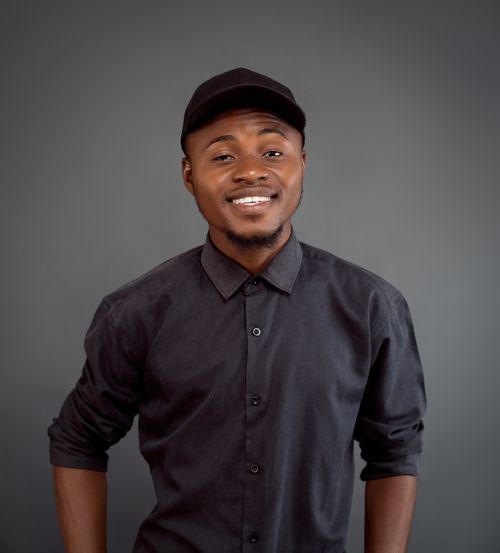 Free Confident young man in a black shirt and cap smiling against a grey studio background. Stock Photo