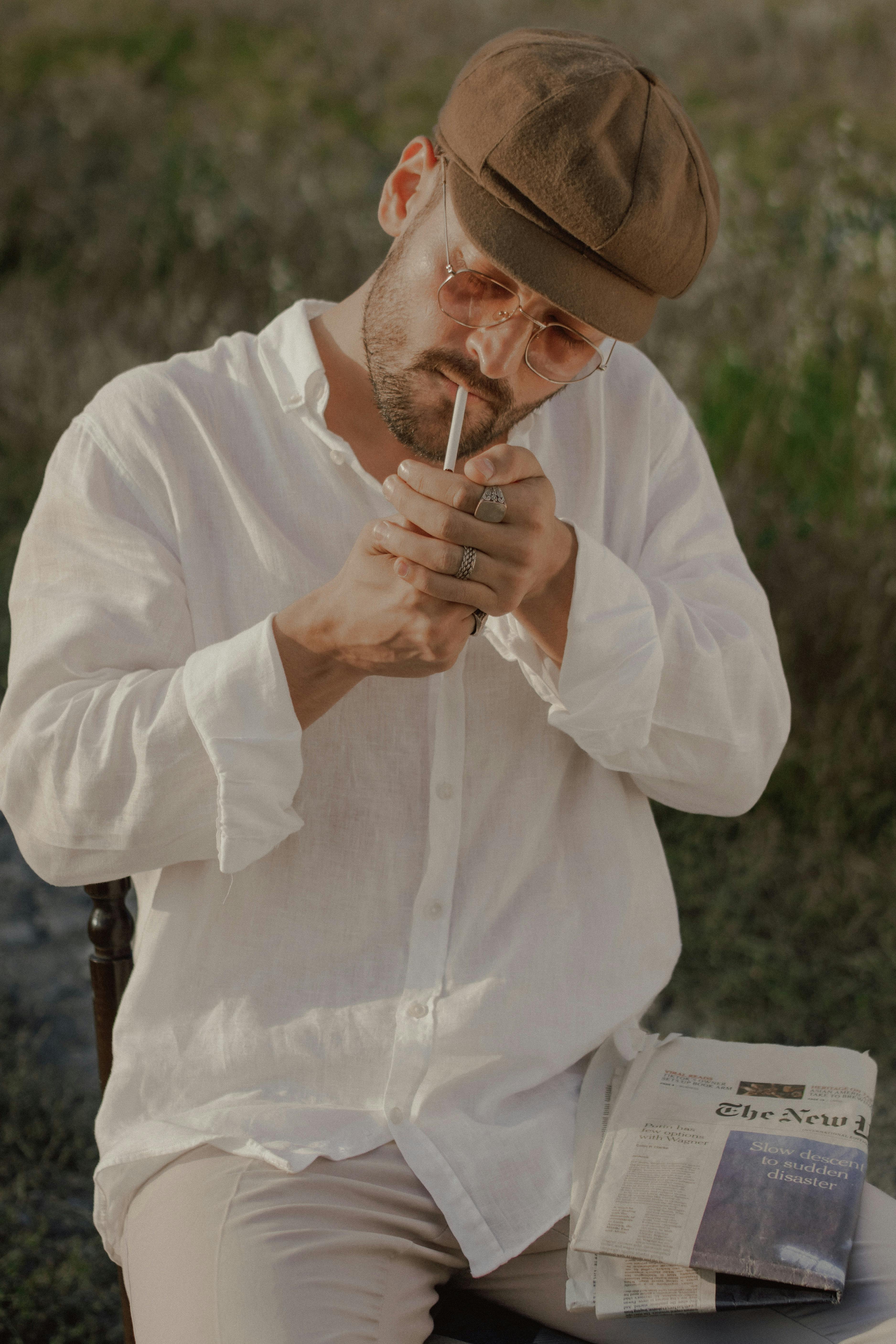 a man in a hat and white shirt smoking a cigarette