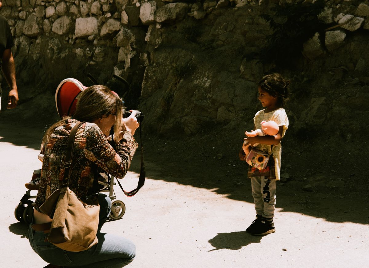 Photographer sitting and photographing a toddler outdoors