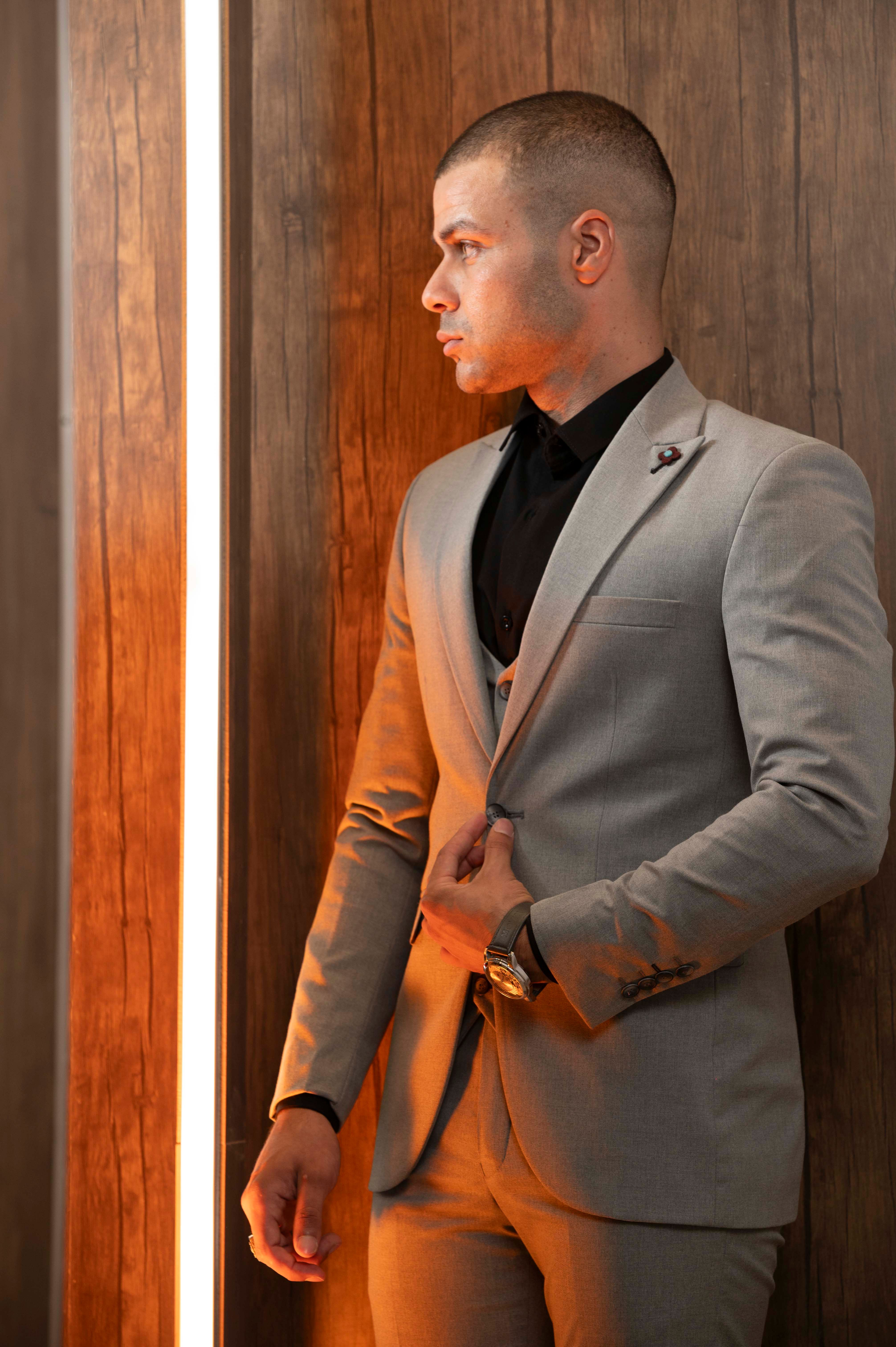 Fashionable man wearing a gray suit standing against a warm-lit wooden wall, creating a modern look.