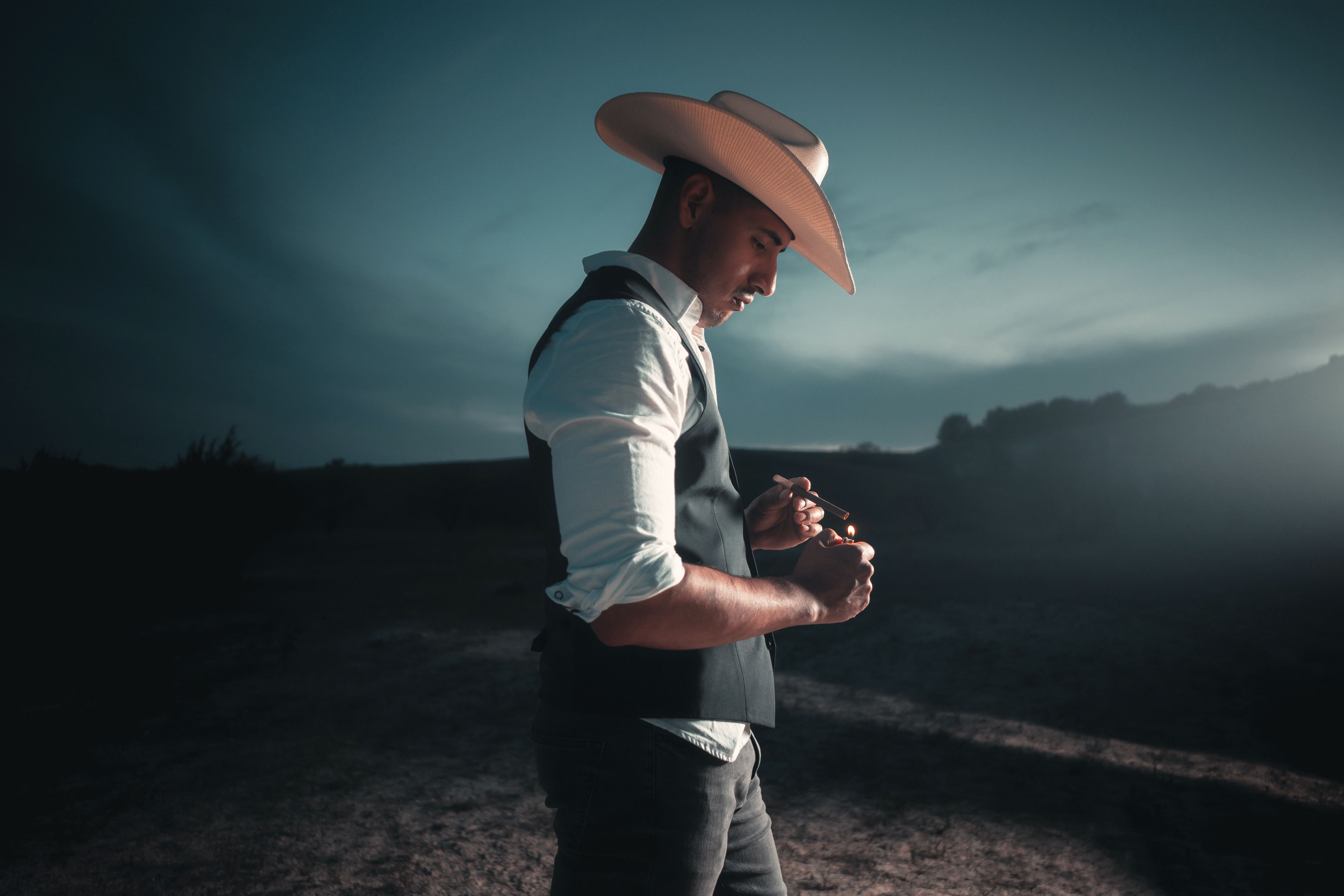 A man in a cowboy hat and vest stands outdoors at dusk in San Antonio, Texas.