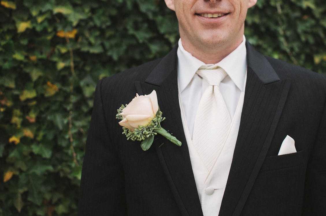 Man in Black Formal Suit With White Necktie Beside Green Bush in Shallow Focus Photography