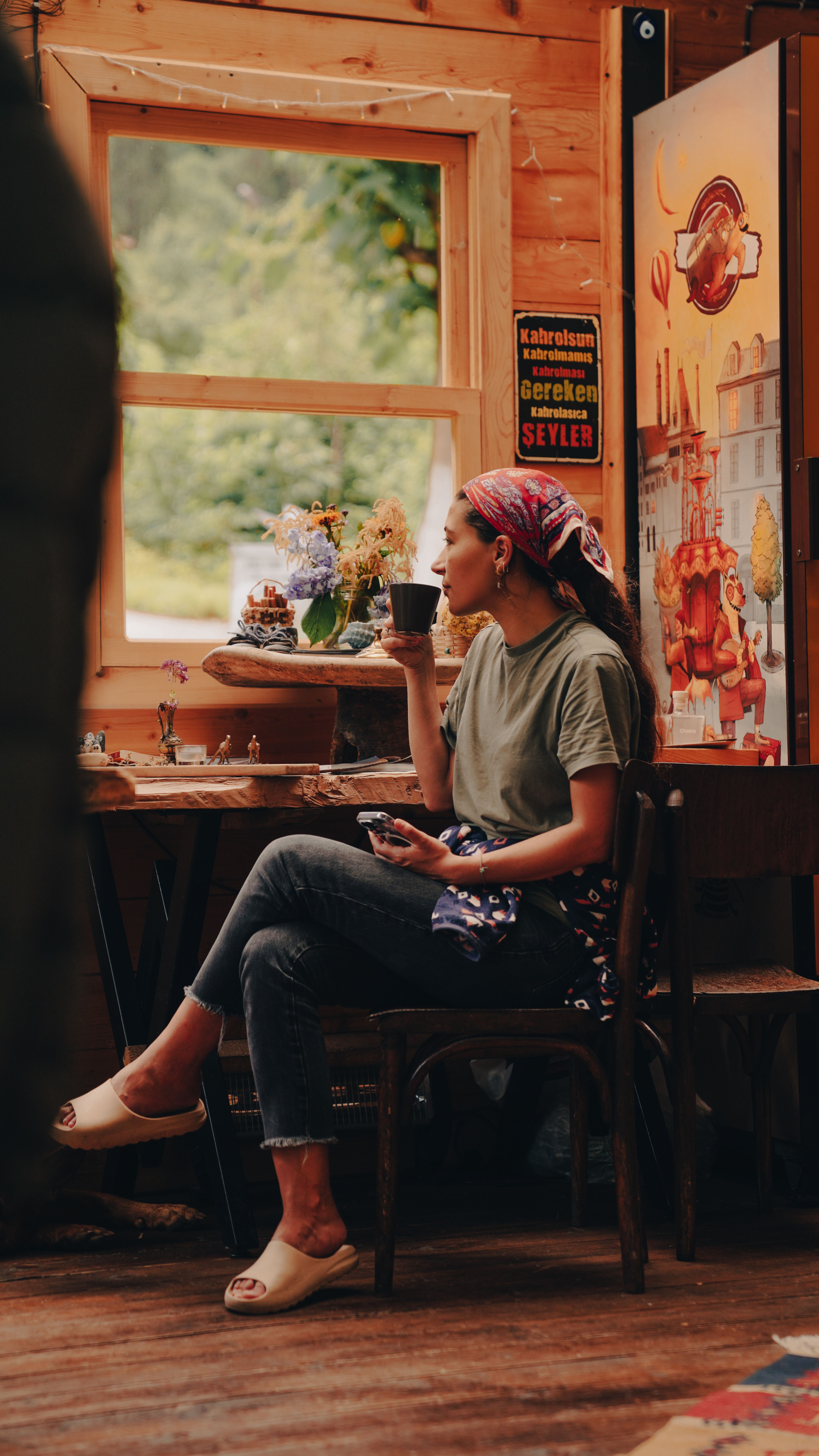 Young woman enjoying coffee indoors, embracing cozy wooden ambiance in casual attire.