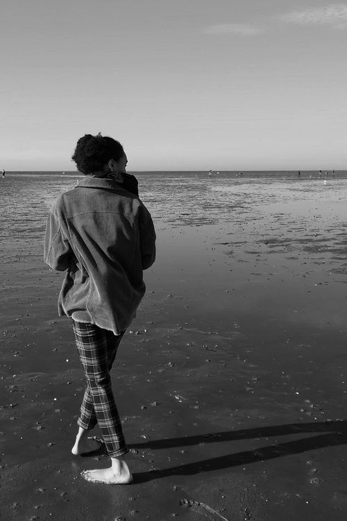 Free A serene black and white photo of a woman walking barefoot on the beach, enjoying a quiet moment by the sea. Stock Photo