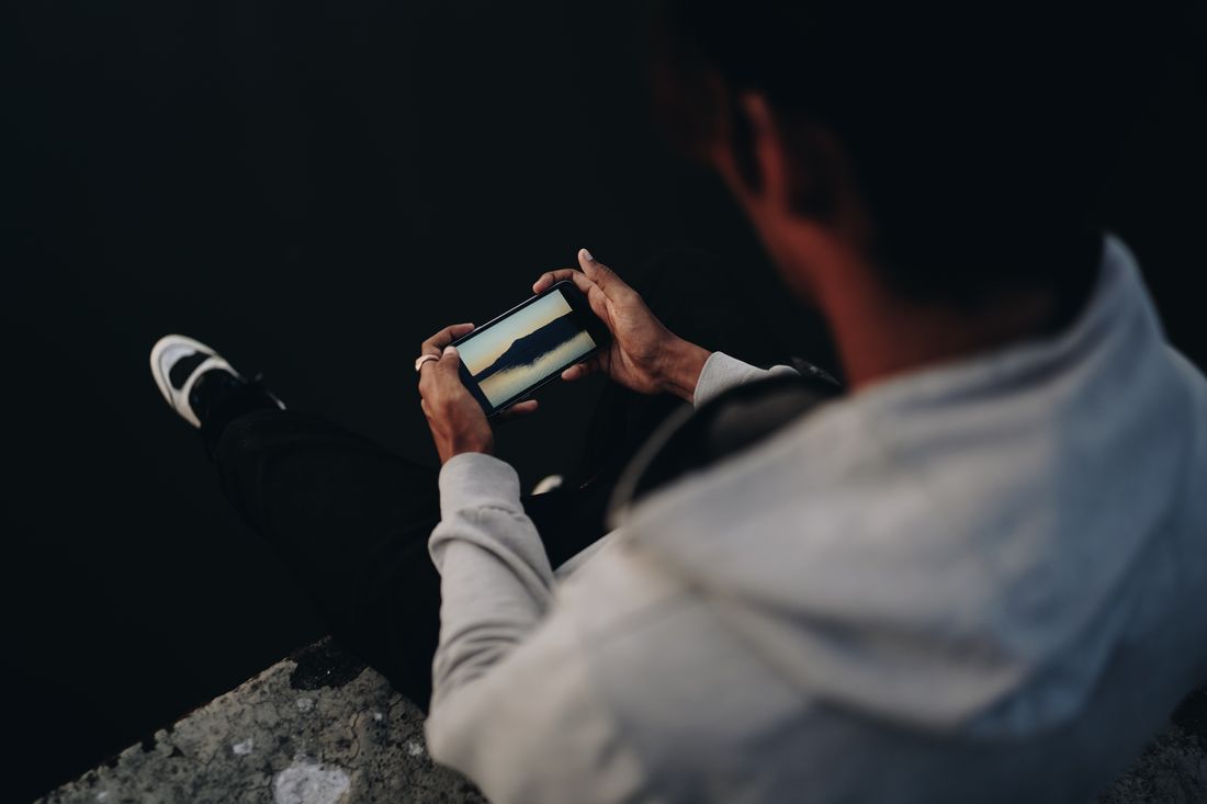 A man on a ledge at night watching video on a phone