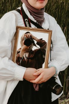 Woman holding mirror with reflected photographer in artistic outdoor shot.