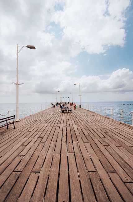 A scenic view of people walking on a wooden pier in Limasol, Cyprus, overlooking the sea.