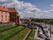 View of a historic castle near a city road with traffic and pedestrians.