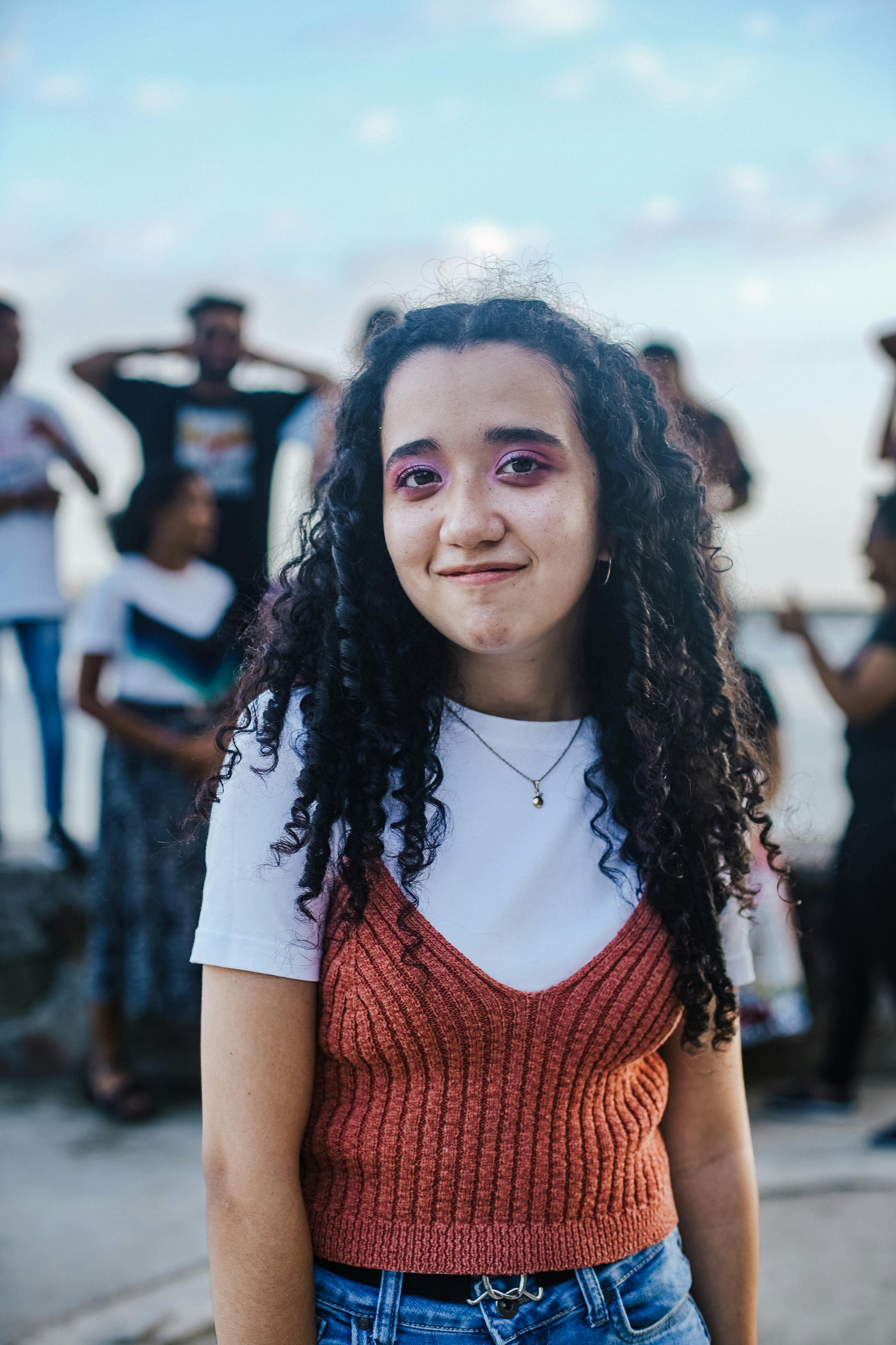 Young woman with curly hair and colorful makeup outdoors, casual setting.