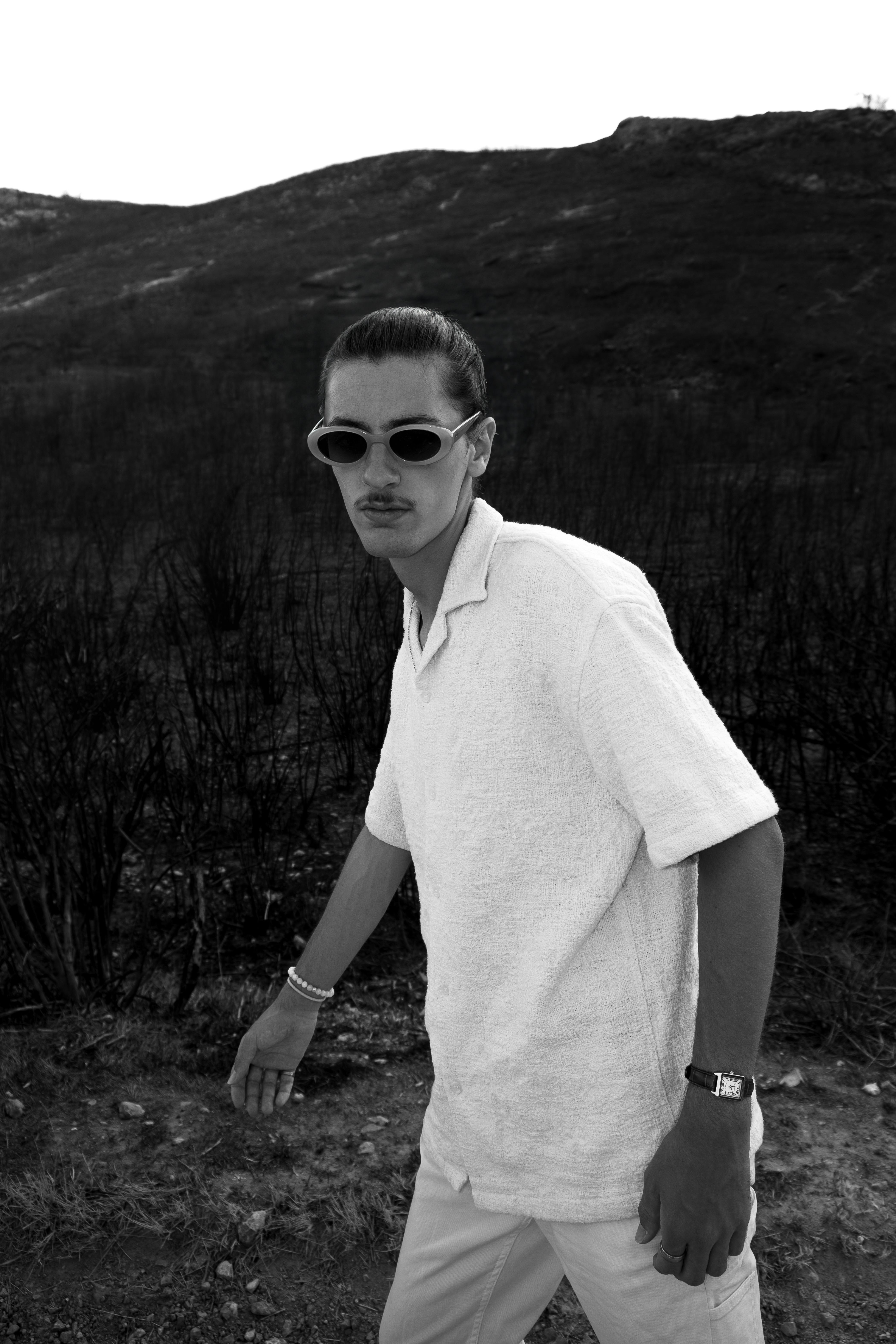Free A fashionable man in sunglasses poses in a scenic outdoor setting, captured in black and white for a modern aesthetic. Stock Photo
