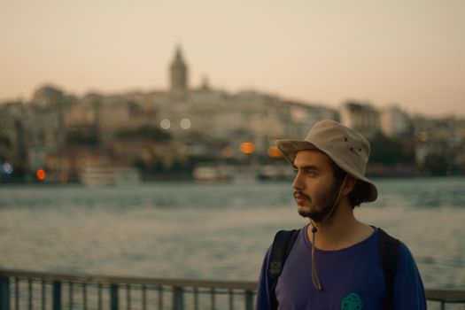 Young man in hat with backpack exploring Istanbul skyline during sunset.