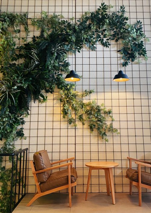Free Inviting café corner with lush ivy, wooden armchairs, and warm lighting. Stock Photo