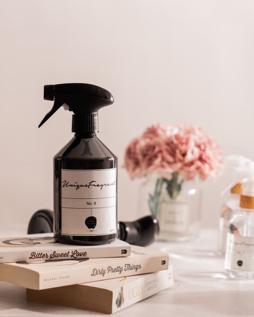 Free A sleek black spray bottle on books surrounded by pink flowers. Stock Photo