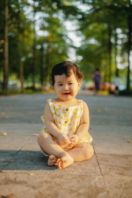 Free Happy child in a yellow sundress smiling while sitting on park pavement in Bắc Giang, Vietnam. Stock Photo