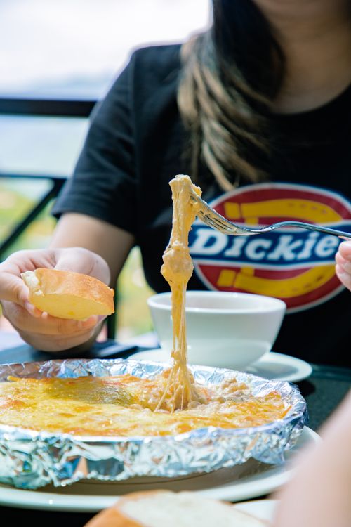 Free A person serving gooey cheese from a dish with bread, creating an appetizing meal scene. Stock Photo