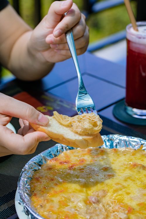 Free Close-up of hands serving cheese dip onto bread alongside a refreshing drink. Stock Photo