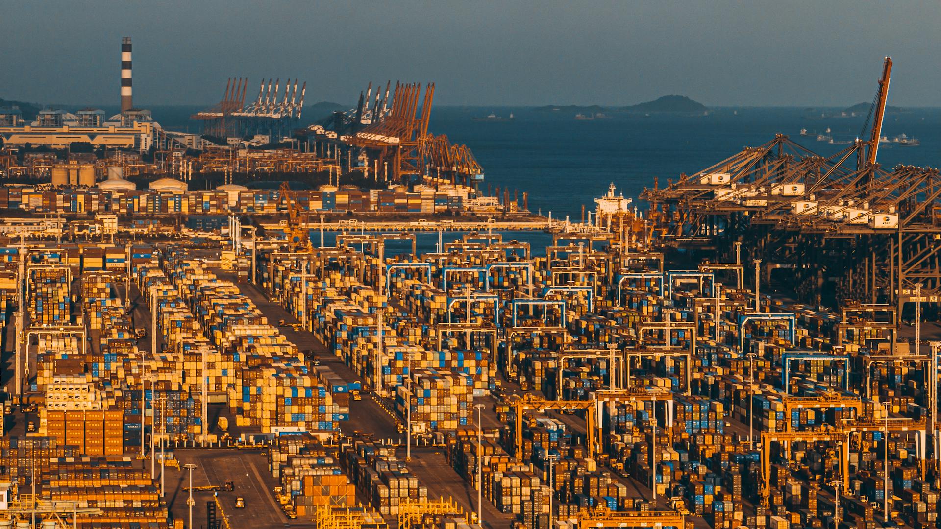 Aerial shot of Xiamen's bustling port with stacked shipping containers and cranes.