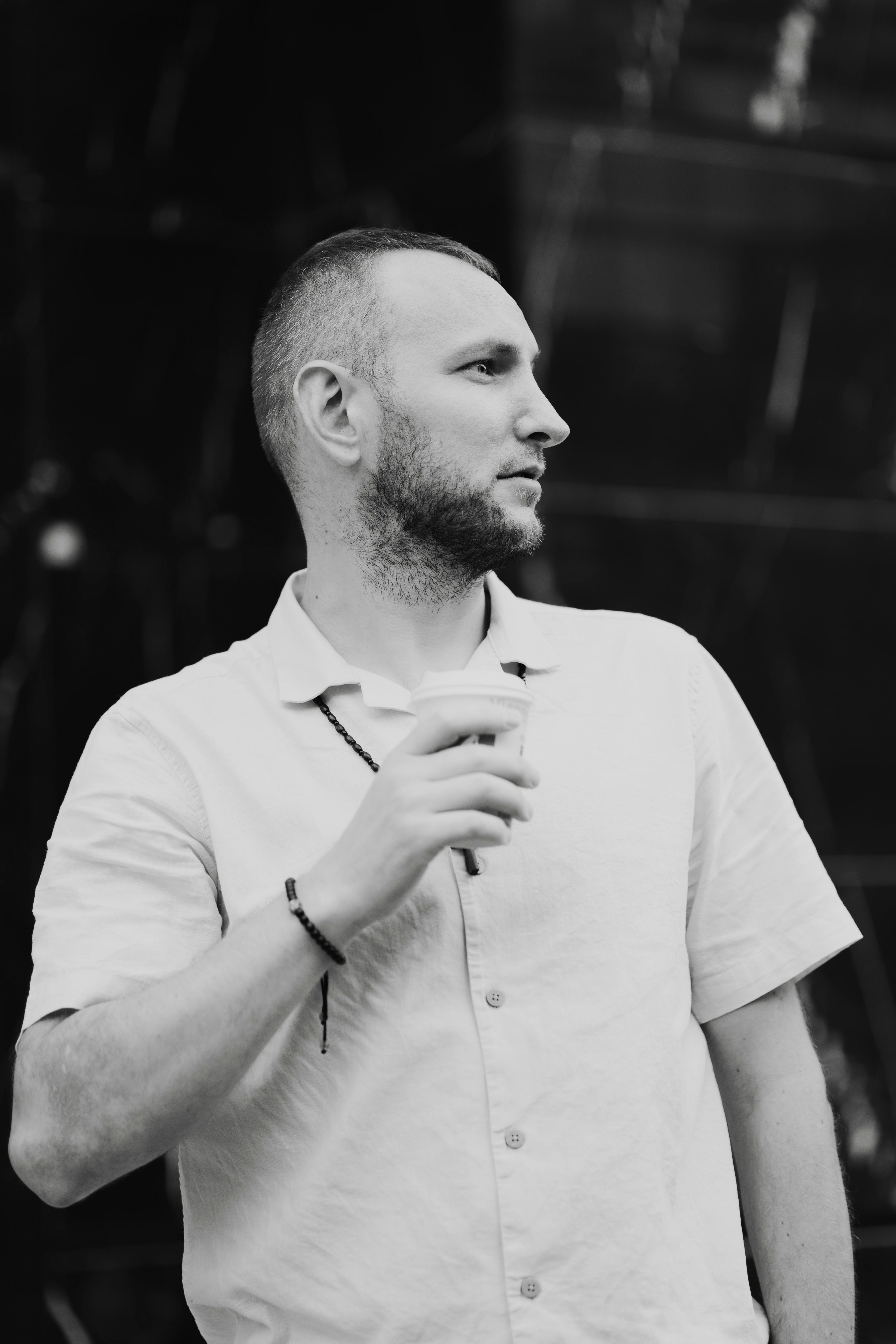 A stylishly dressed man drinks a coffee outside. Black and white portrait.