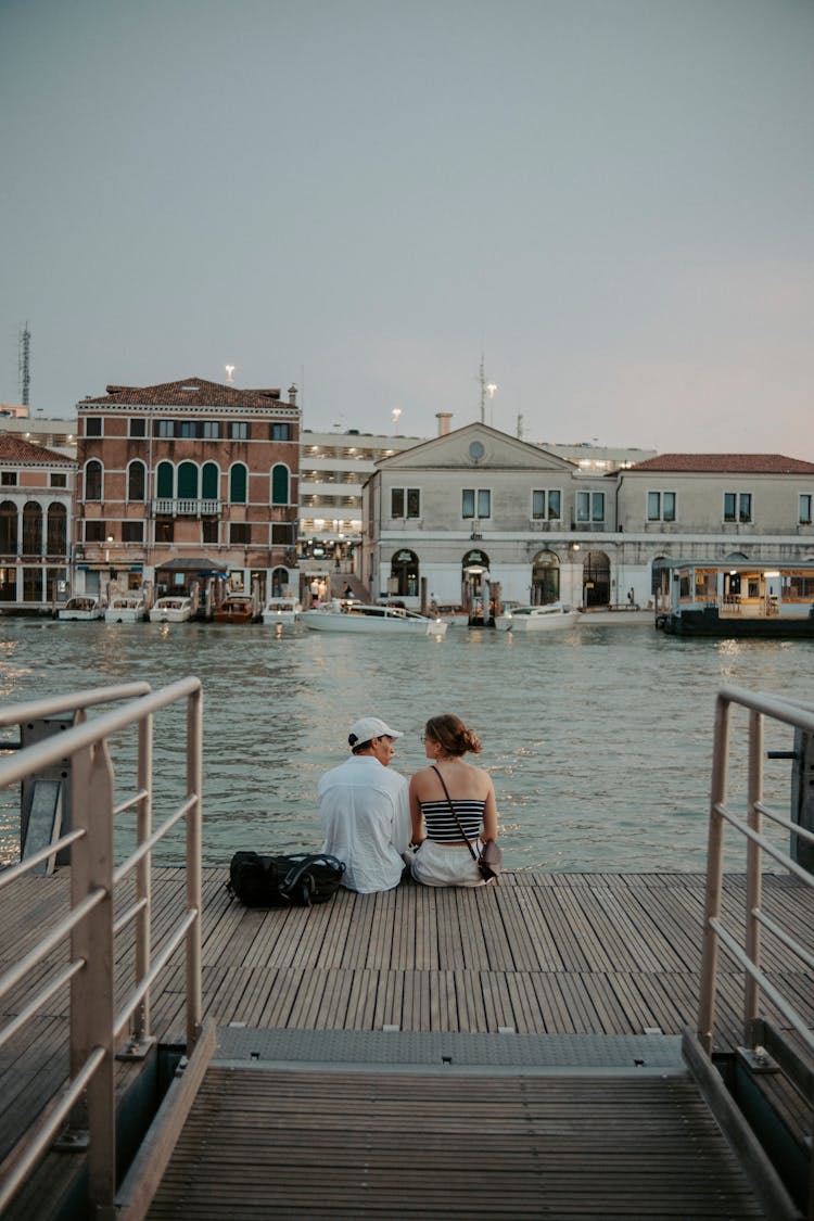 Young Couple Sitting On Boardwalk Near Canal