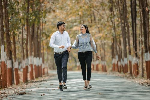 Free Smiling couple holding hands and walking down a tree-lined road, enjoying a sunny day in the park. Stock Photo