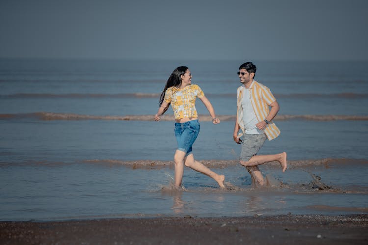 A Young Man And Woman Running On The Seashore 