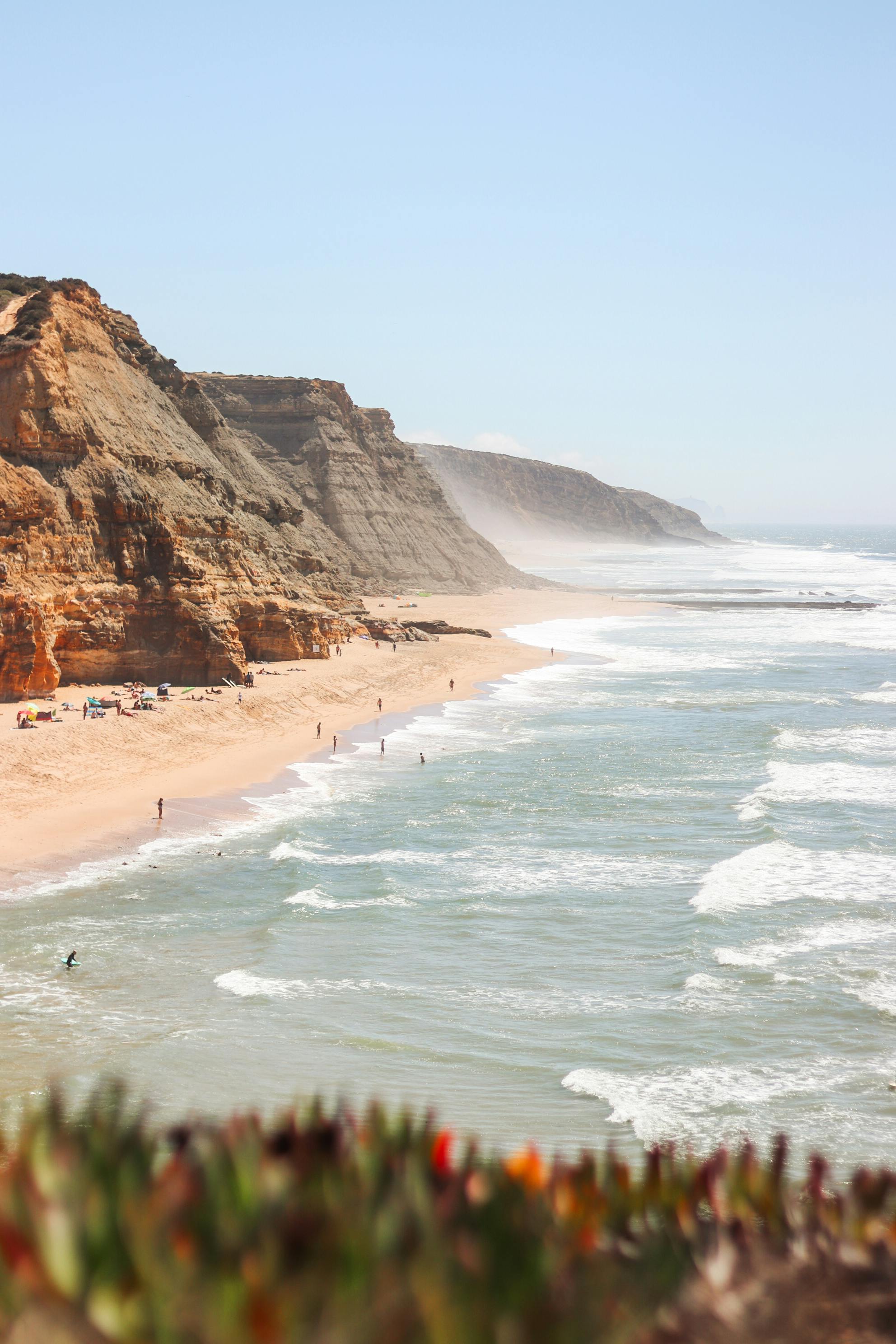 Breathtaking view of Portugal's rugged cliffs and sandy beach along the Atlantic Ocean, perfect for summer travel.