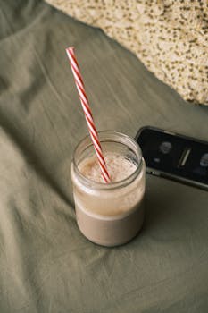 Close-up of a creamy beverage in a jar with a striped straw on a textured surface.
