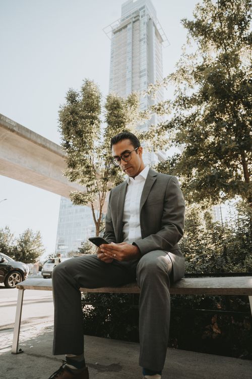 Free A man in a suit sitting on a bench in the city, using his smartphone. Stock Photo