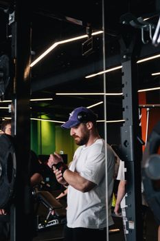 A muscular man adjusts his wrist wraps at a gym, preparing for a workout session.